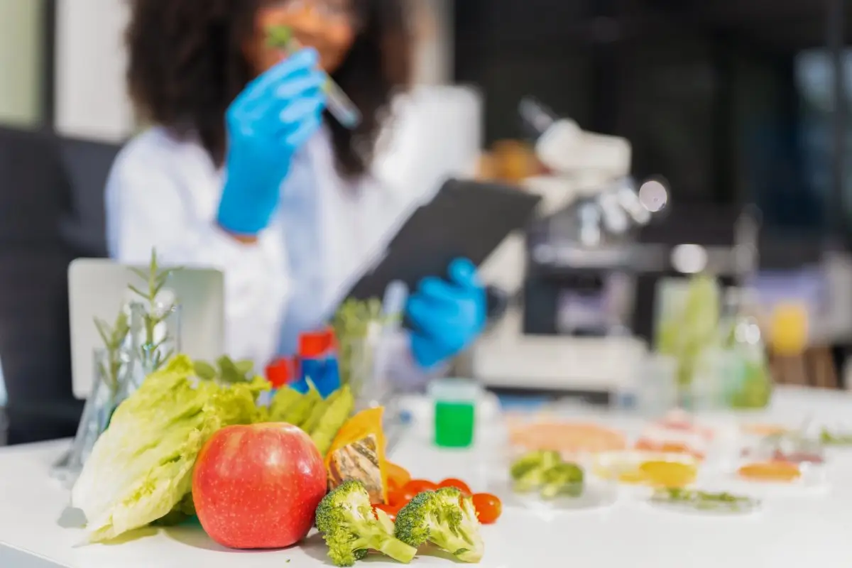 Profissional em laboratório com alimentos frescos e equipamento de análise, simbolizando testes genéticos ligados à nutrição.